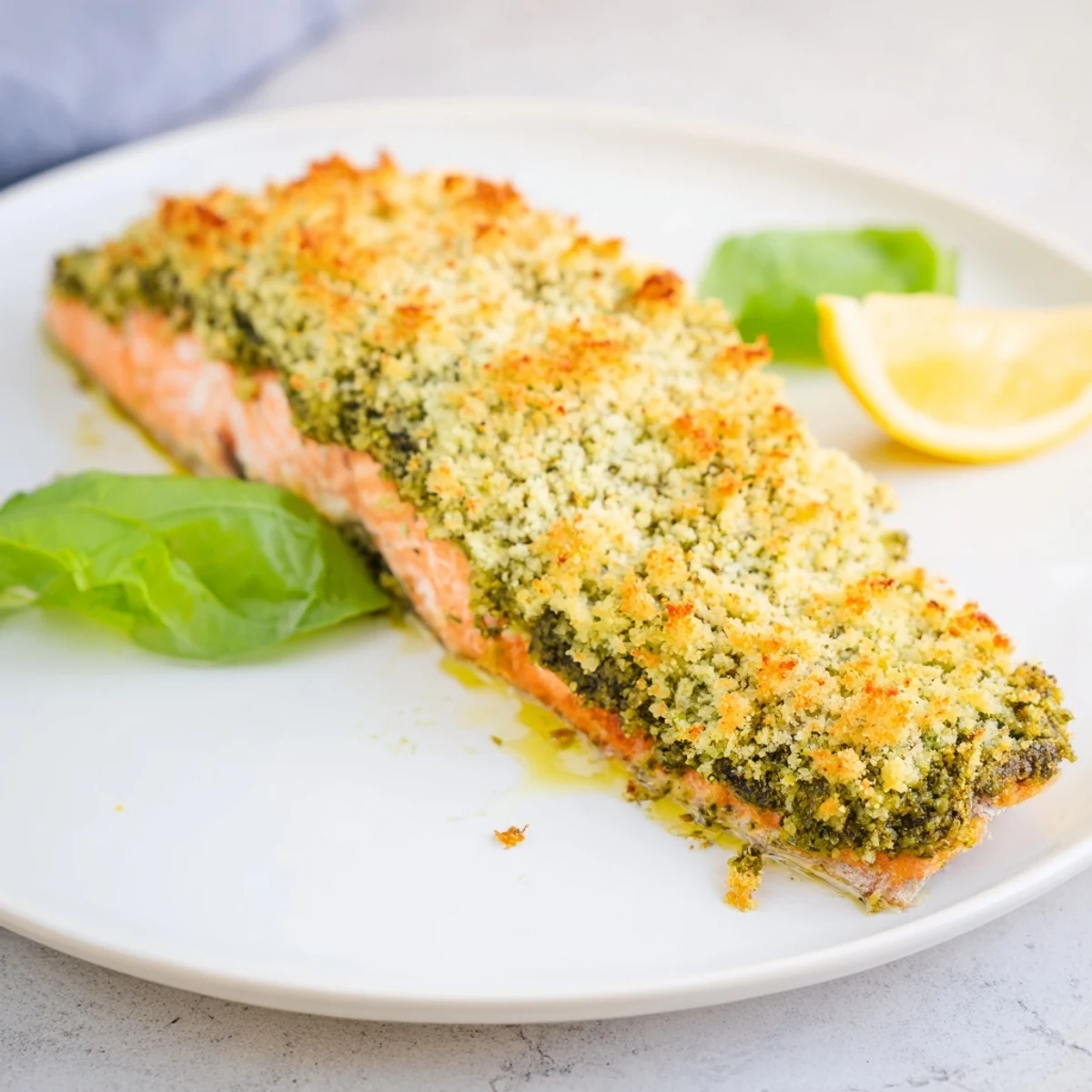 Perfectly cooked Baked Salmon with Pesto Crust, served with lemon wedges and fresh basil.