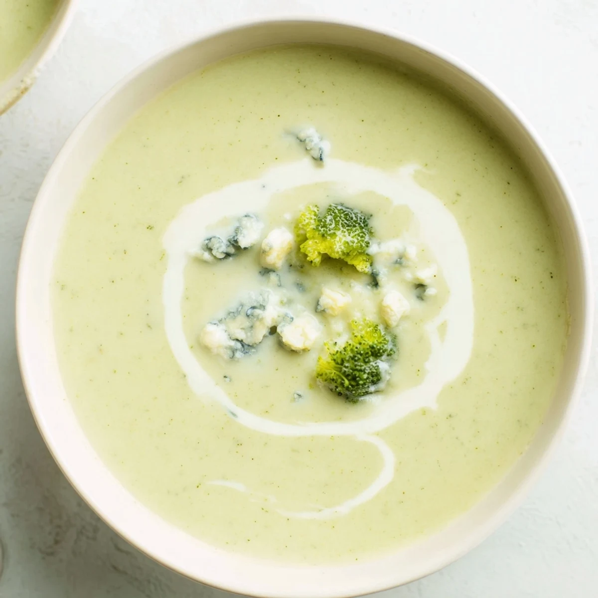 Creamy Broccoli and Stilton Soup, swirled with cream, is served in a bowl, perfect for a cozy supper.