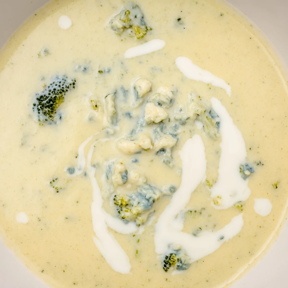 A steaming bowl of Creamy Broccoli and Stilton Soup, garnished with crumbled cheese, smells fragrant and delicious.