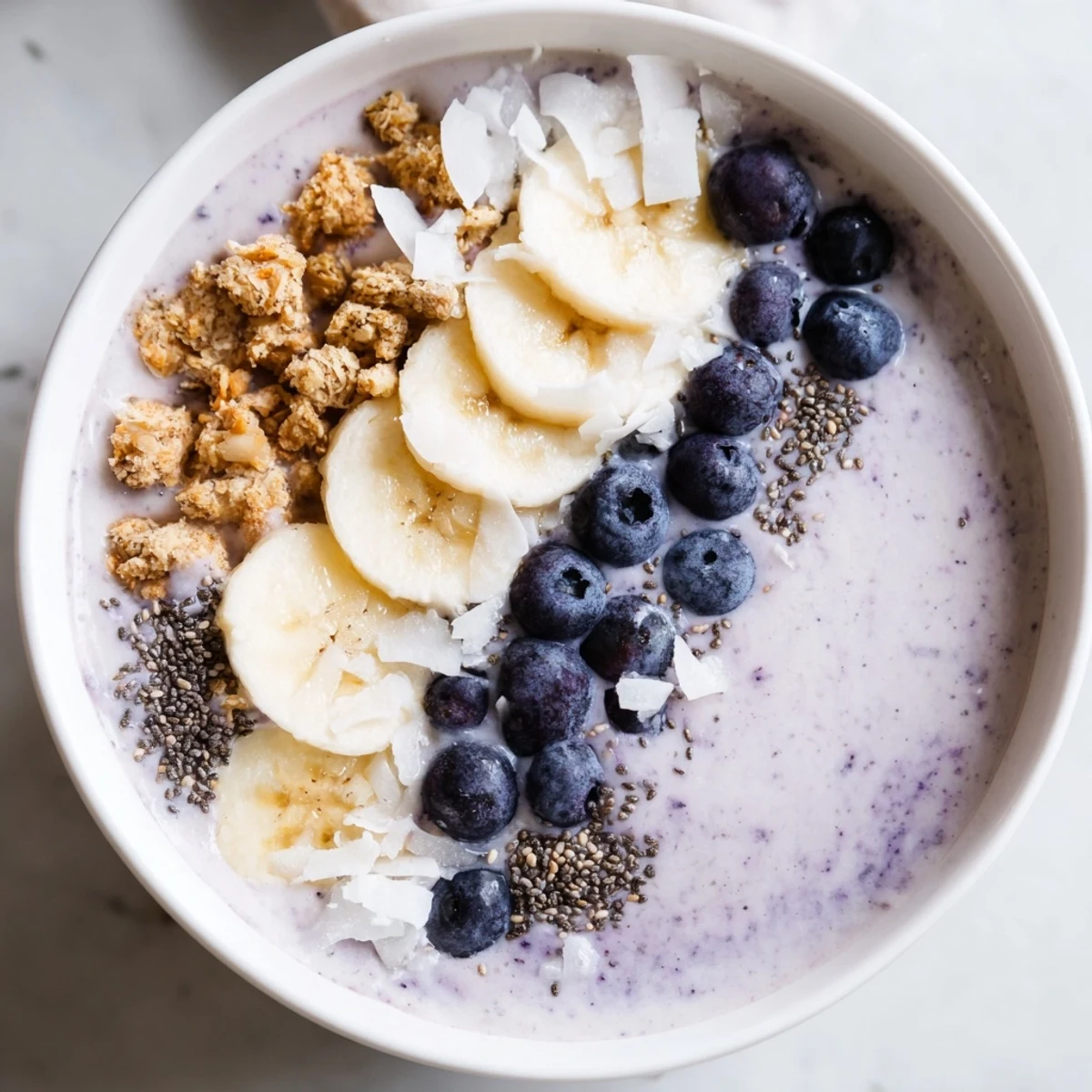 Creamy lemon blueberry smoothie bowl topped with fresh fruit, granola, and chia seeds for a healthy breakfast.