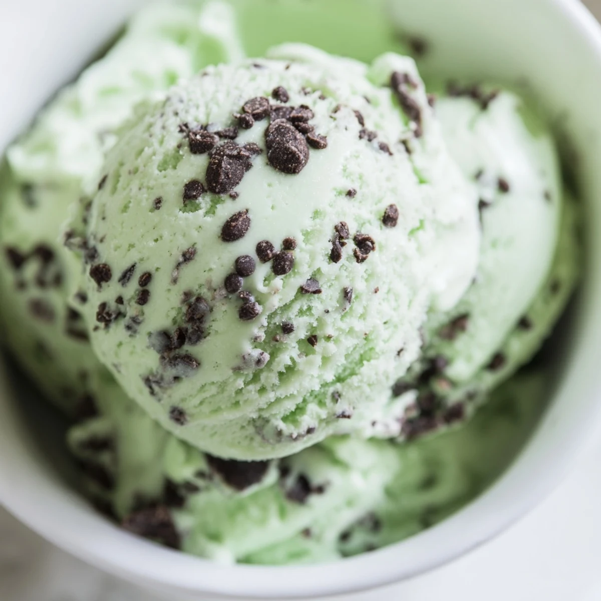 A vintage ice cream scoop lifts creamy peppermint ice cream with chocolate chips from a white bowl.