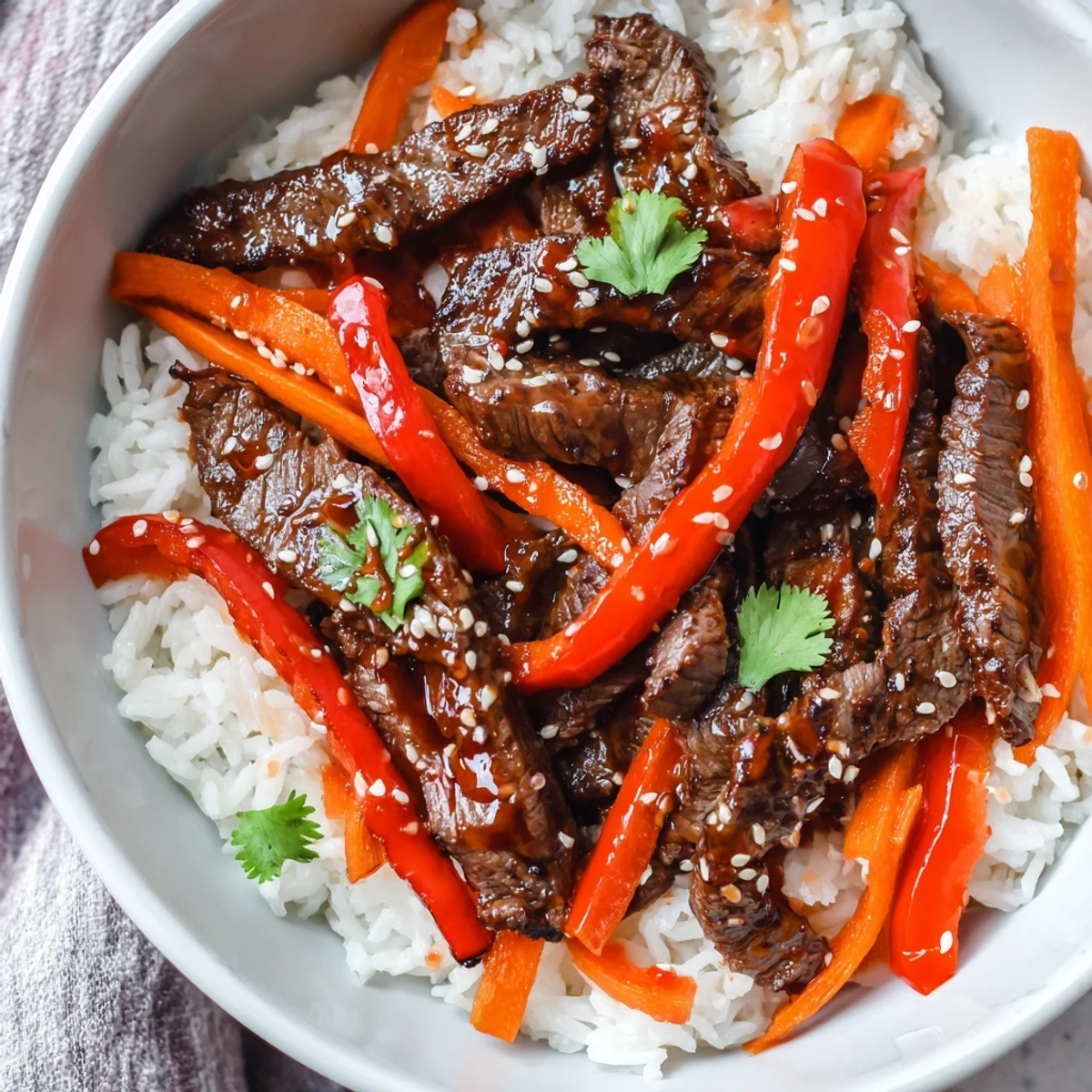 A close-up of the Spicy Beef Bowl, showcasing glossy, tender beef strips glistening with a bold red sauce nestled in fluffy white rice with crisp snap peas and red bell peppers.