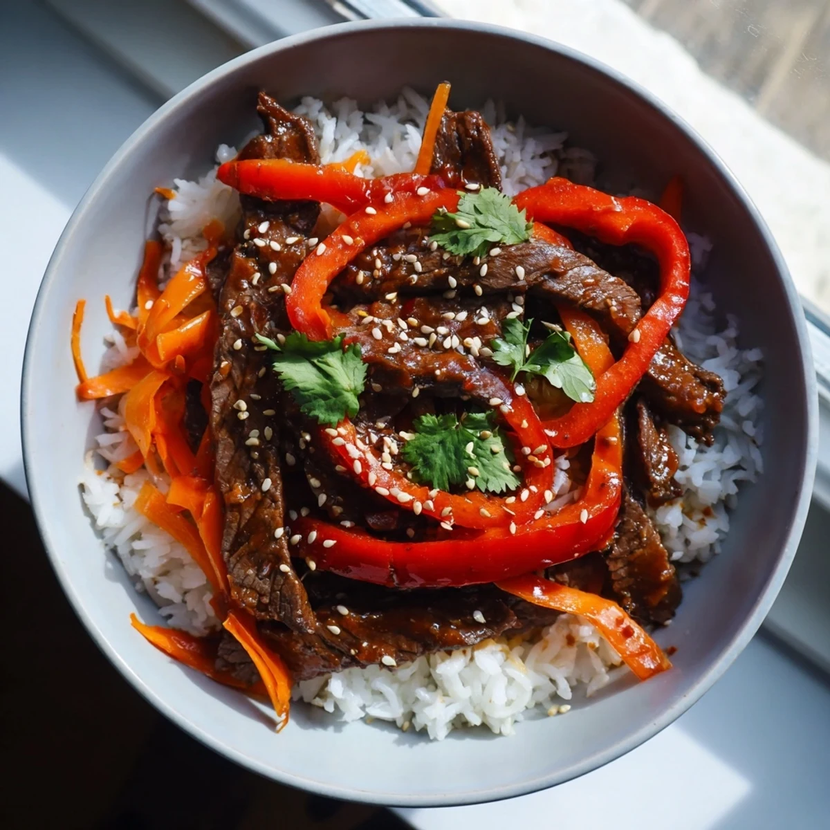 Overhead shot of the Spicy Beef Bowl, featuring a colorful mound of rice topped with sautéed beef and crunchy vegetables, garnished with fresh cilantro and toasted sesame seeds.