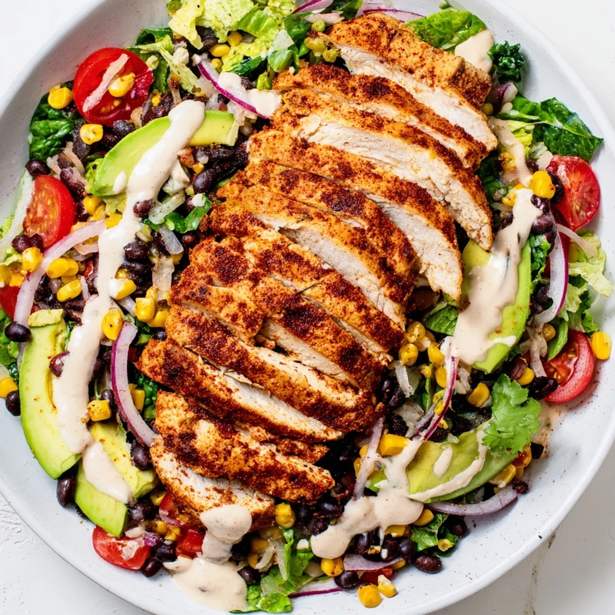 A serving of Southwest Chicken Salad with Chipotle Lime Dressing, featuring grilled chicken slices over greens, black beans, corn, and avocado chunks.