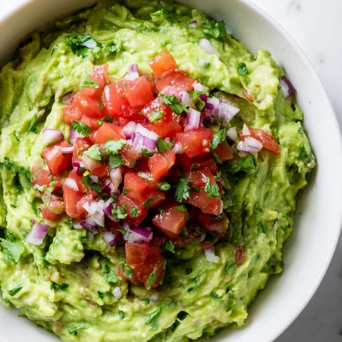 Creamy Game Day Guacamole topped with fresh tomato salsa and chopped cilantro, served with crunchy tortilla chips.