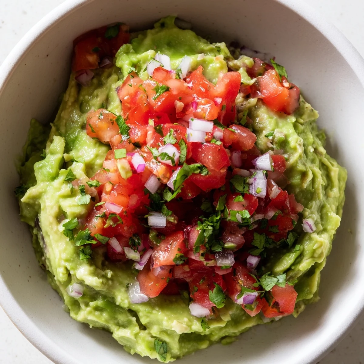 Zesty Game Day Guacamole layered with bright tomato salsa and lime, paired with crispy tortilla chips for dipping.