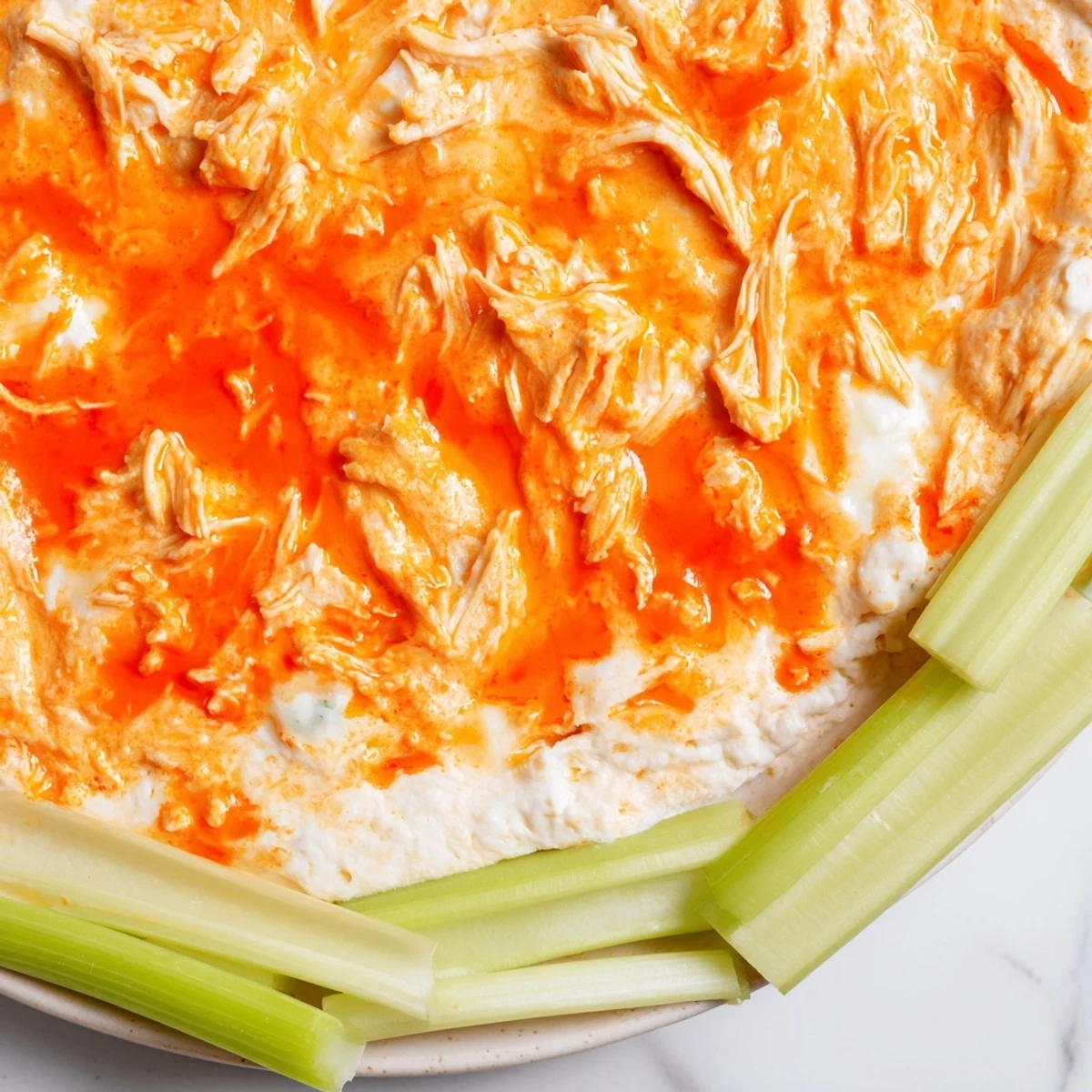Fresh celery sticks ready for dipping into a golden, baked bowl of Spicy Buffalo Chicken Dip.