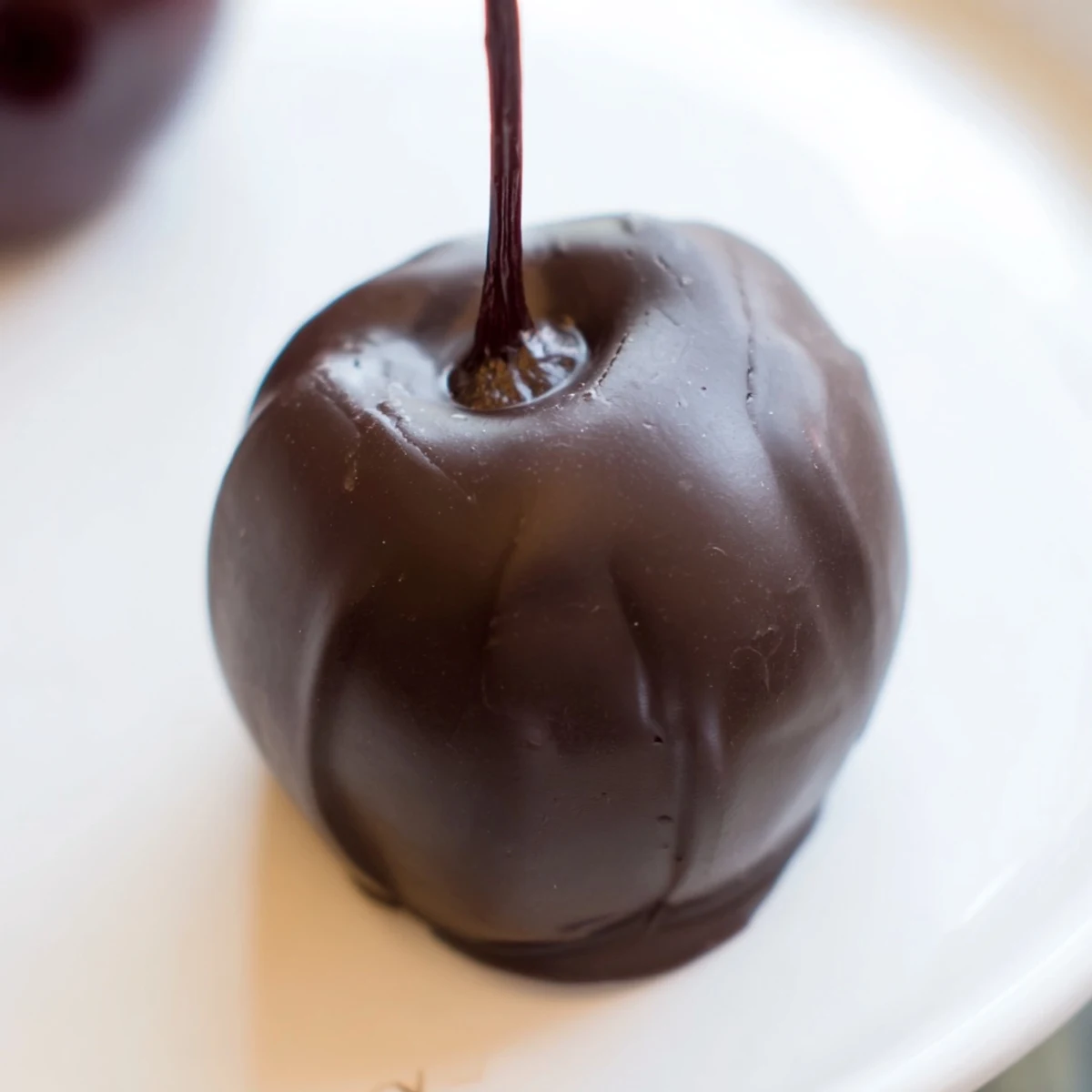 Glossy chocolate covered cherries with a soft fondant center, arranged on a parchment-lined tray for a classic homemade treat.