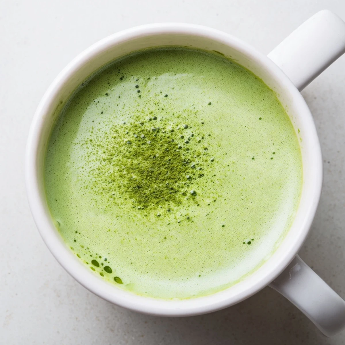Steaming green matcha latte in a clear glass mug, topped with creamy froth and a light dusting of powder.  