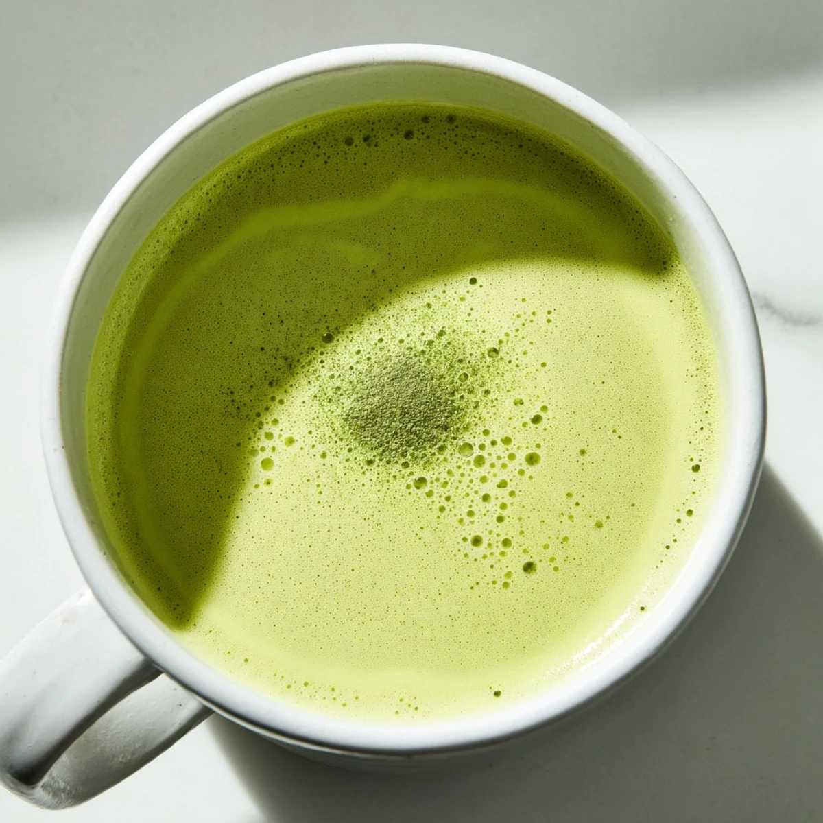 Pouring frothy oat milk into a cup of matcha, creating a creamy swirl for a photogenic latte.