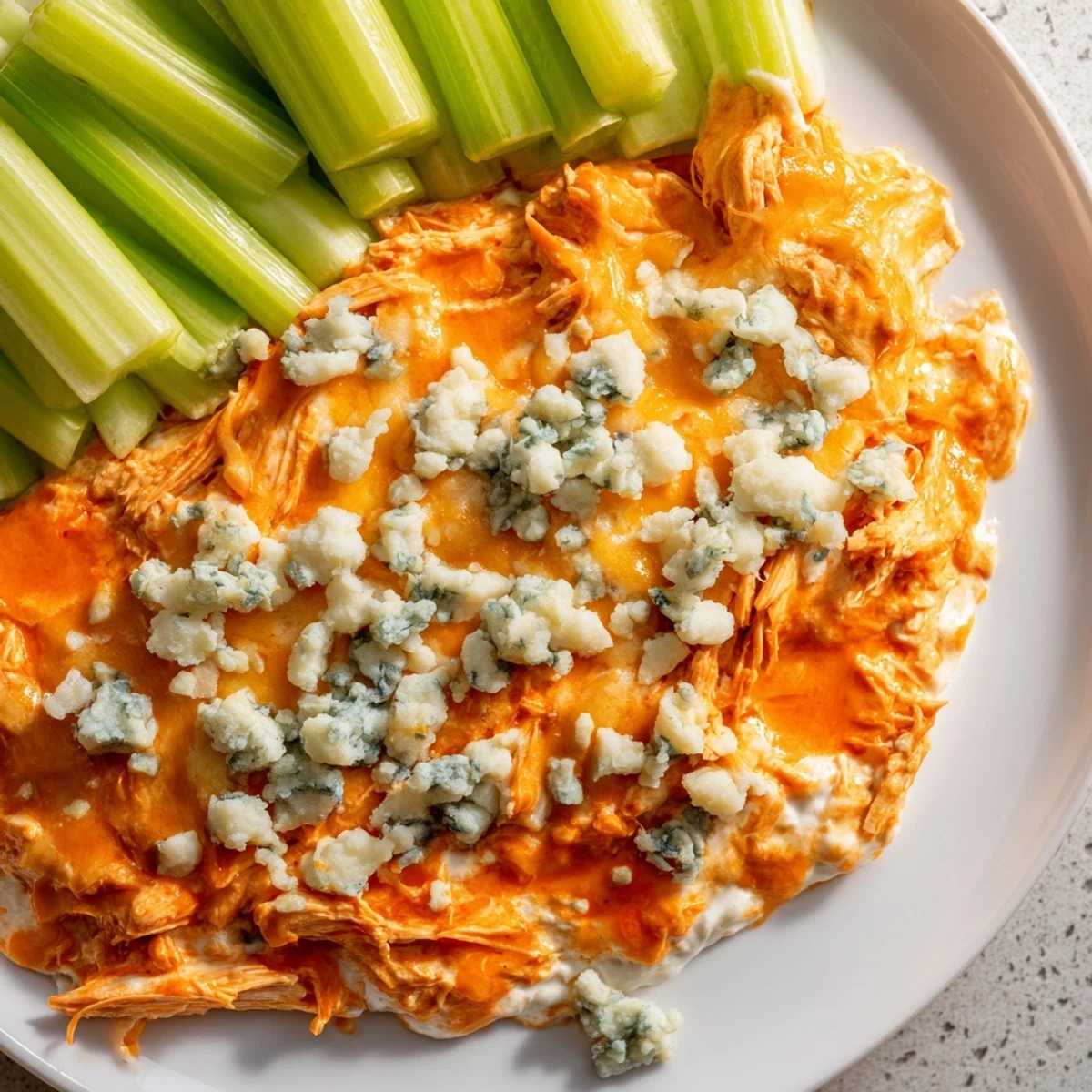 Fresh celery sticks and blue cheese crumbles garnish this golden, bubbling Spicy Buffalo Chicken Dip served warm in a rustic baking dish.