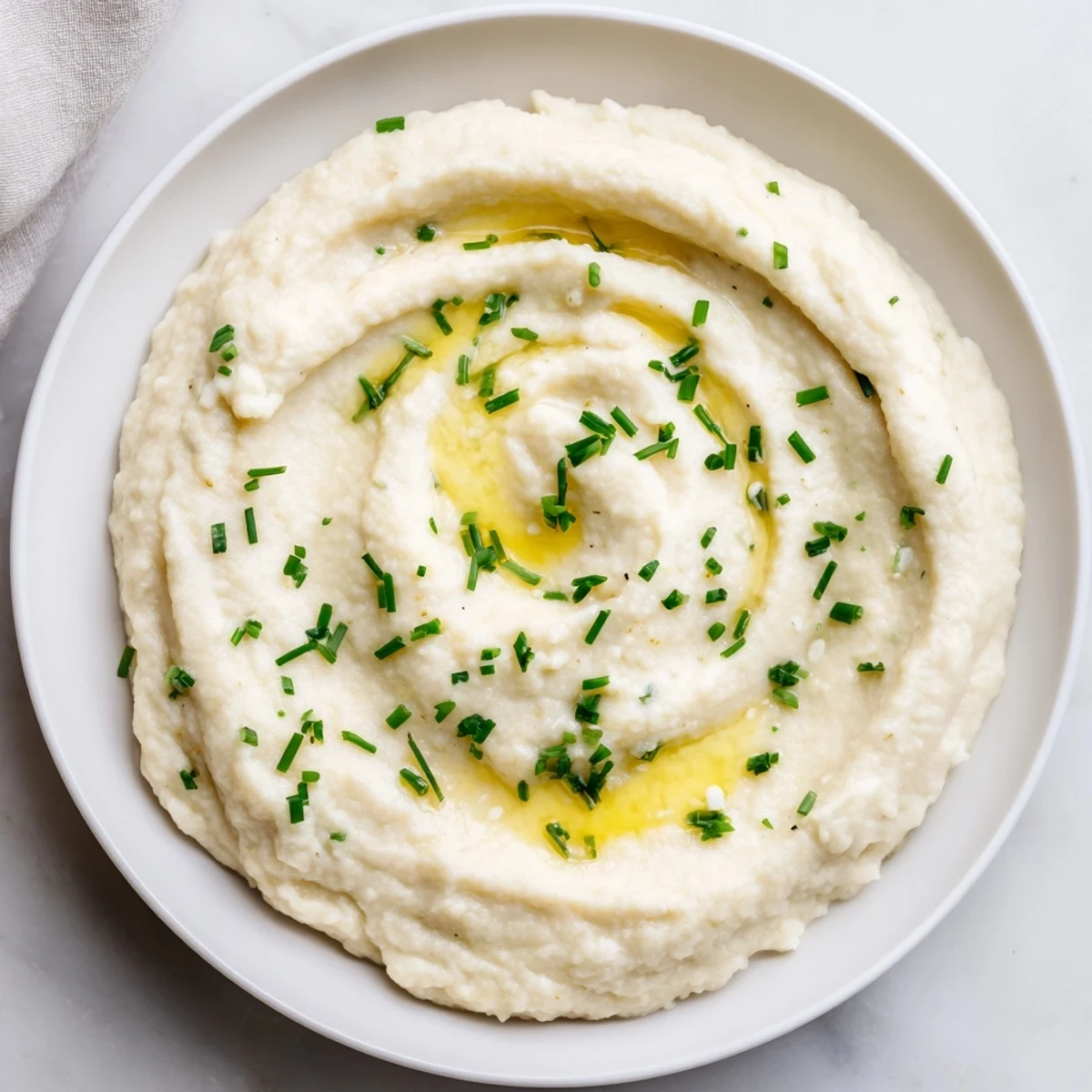 A food processor blends Roasted Garlic Mashed Cauliflower to a fluffy, smooth texture for a healthy, low-carb alternative to potatoes.