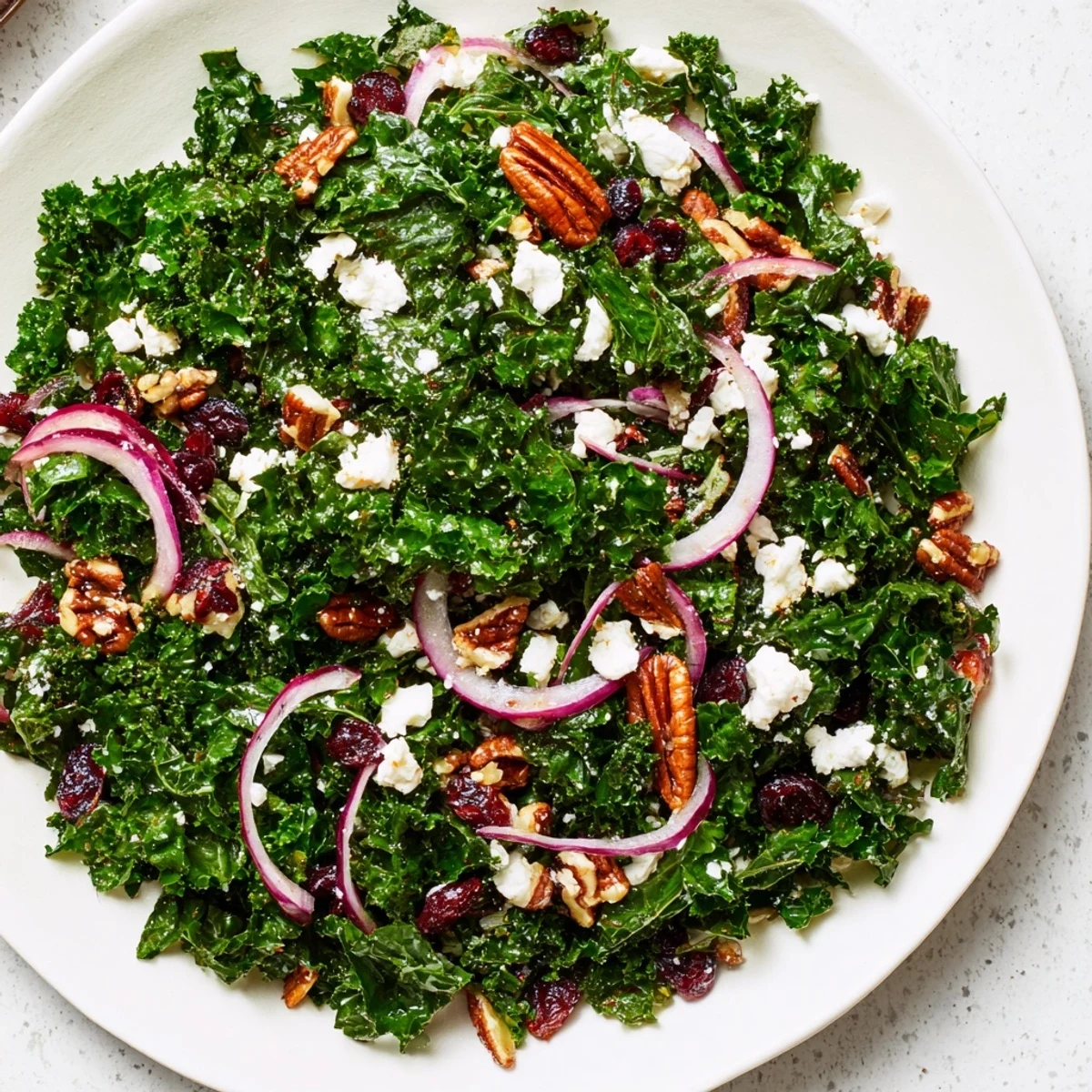 Hearty Winter Kale Salad with Pecans and Cranberries arranged in a rustic wooden bowl, ready to serve. Bright cranberries, sliced red onion, and apple pieces contrast against the dark leafy greens.
