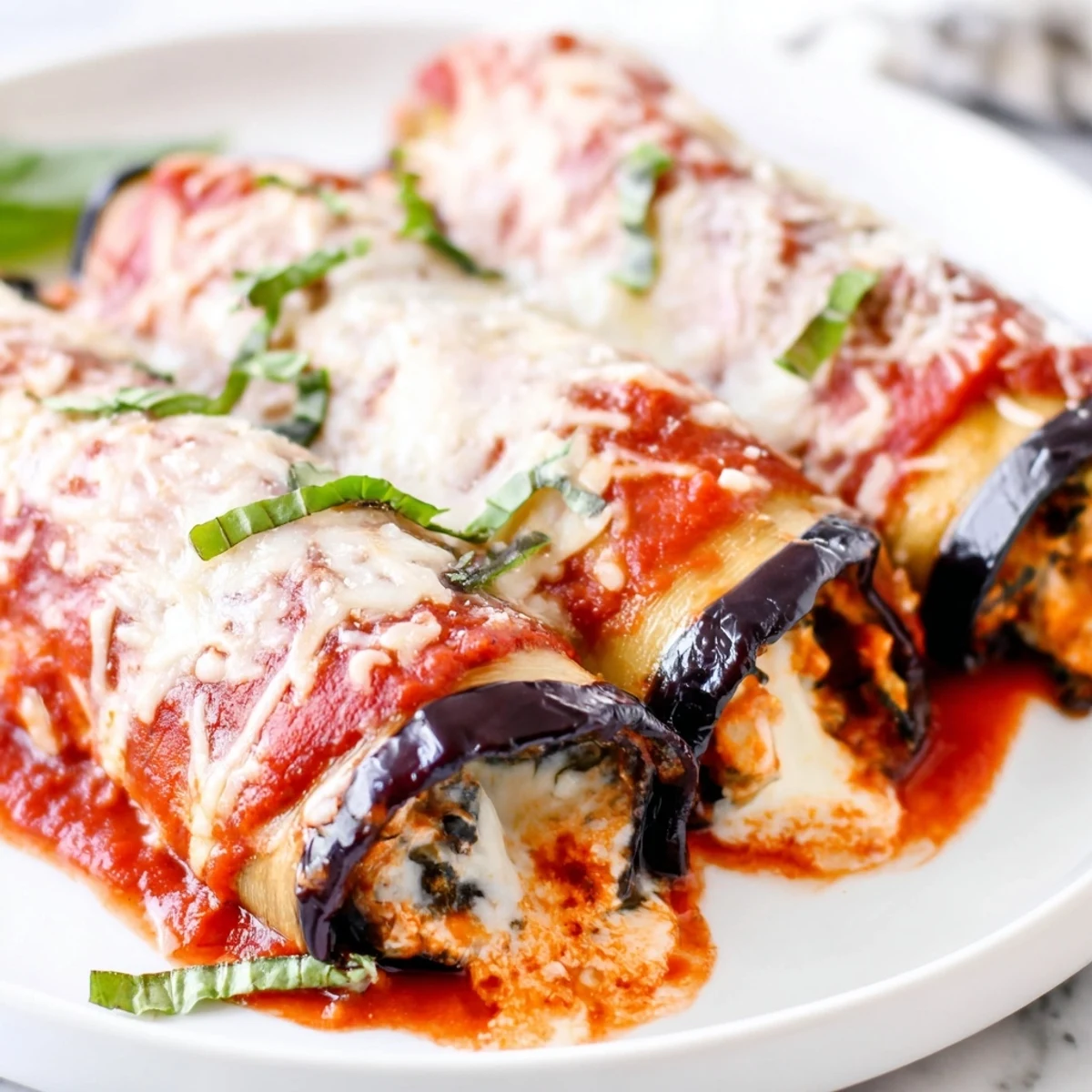A close-up of vegetarian eggplant rollatini shows melted mozzarella, fresh basil garnish, and creamy ricotta.