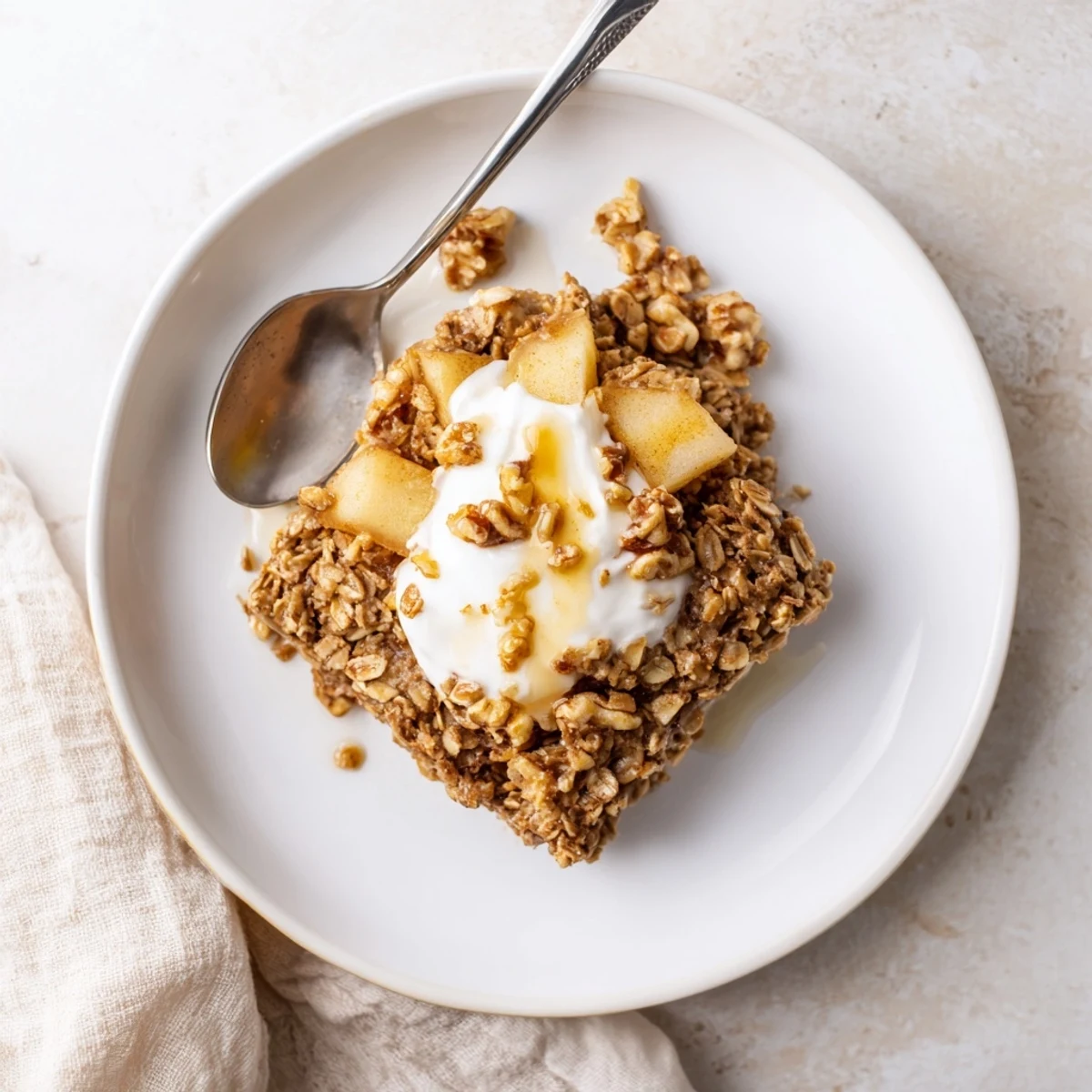 A close-up of baked apple oatmeal with Greek yogurt, showcasing golden oats and tender apple chunks in a rustic baking dish.