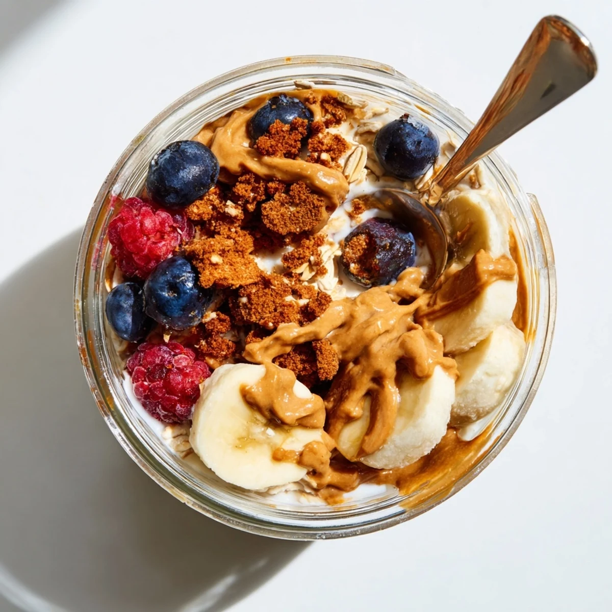 Creamy Quick Biscoff Overnight Oats served in a glass jar, topped with crushed cookies and sliced banana for a sweet breakfast.