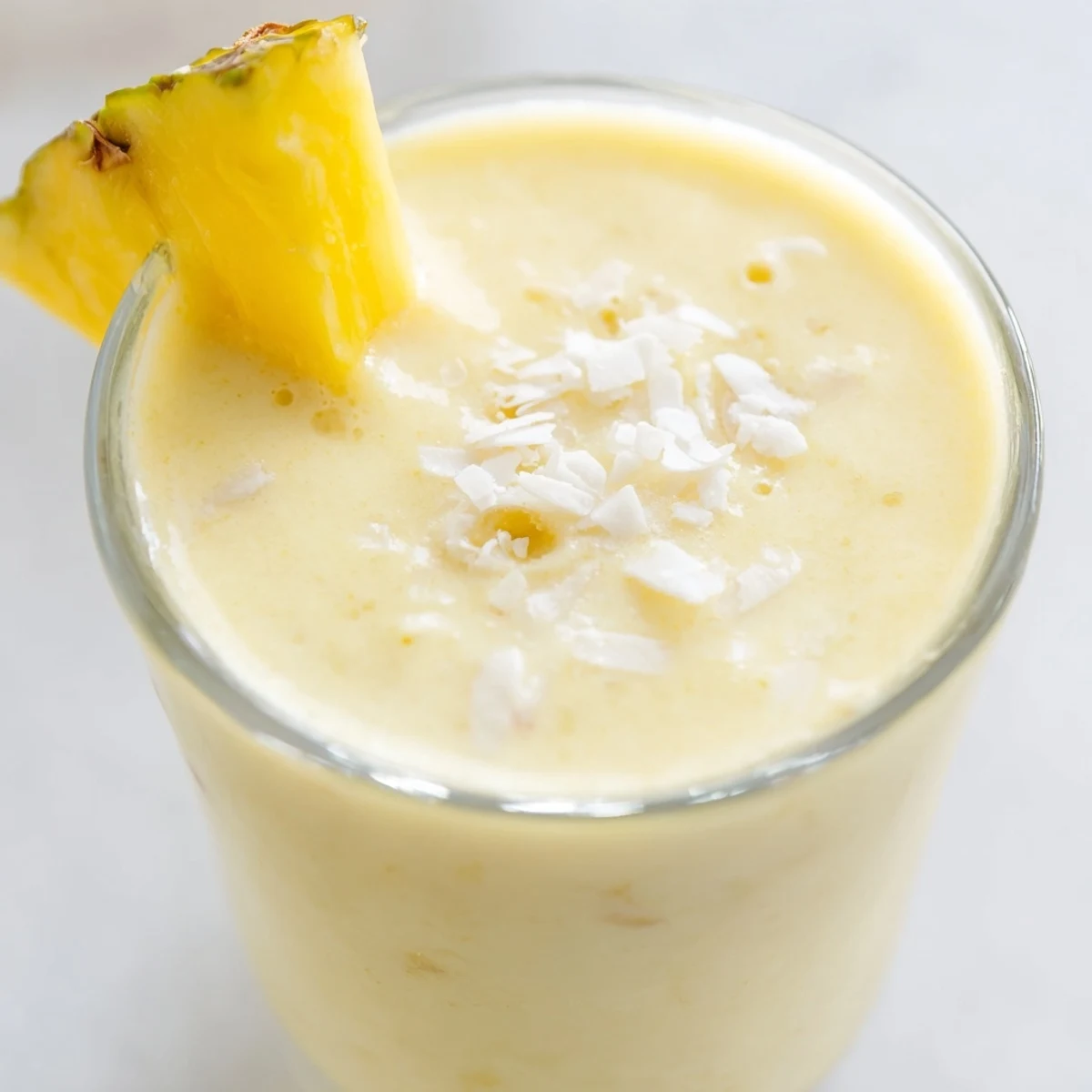 A tall glass of Pineapple Coconut Smoothie topped with shredded coconut, showcasing its creamy texture and tropical garnish.