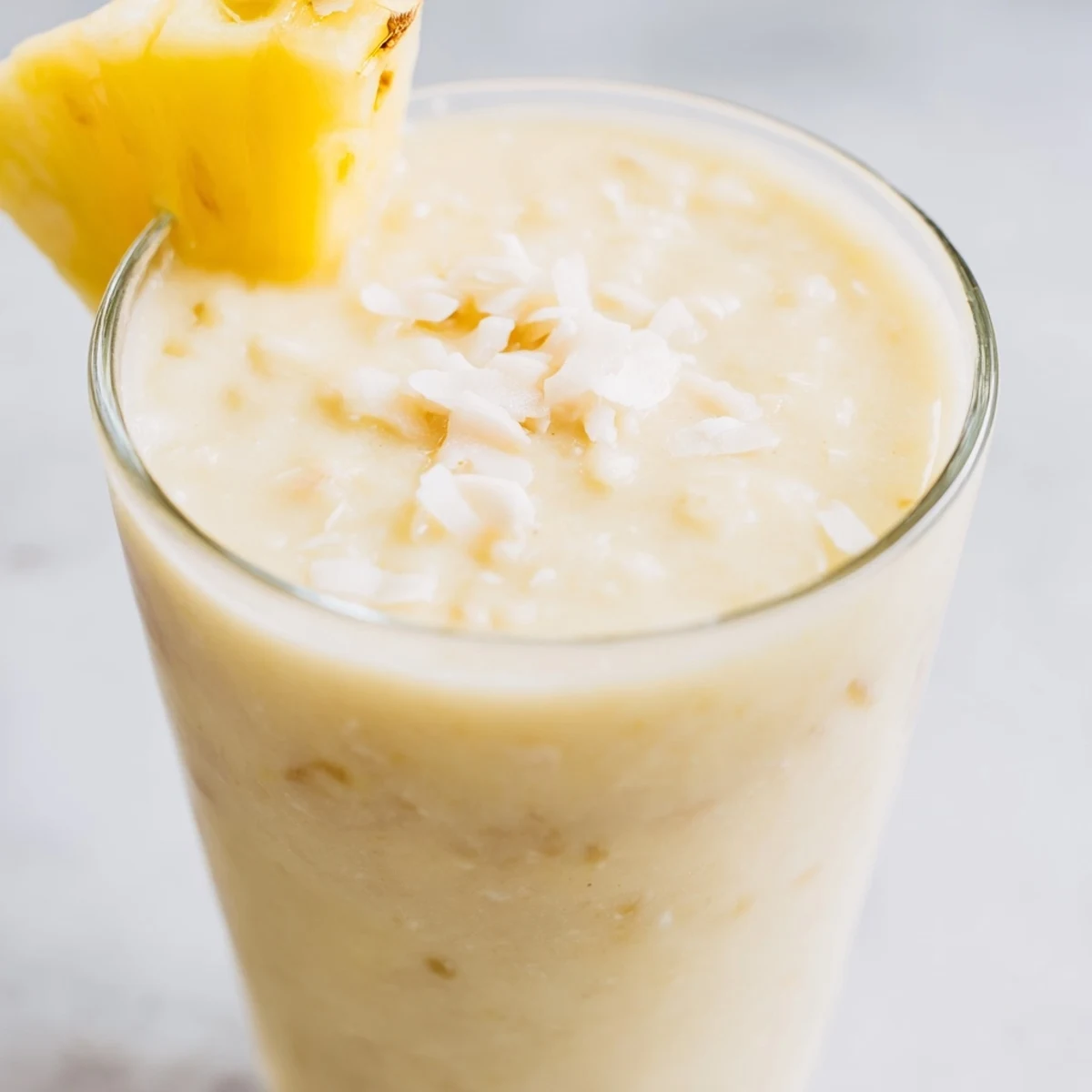 The Pineapple Coconut Smoothie pours smoothly into a glass beside fresh pineapple slices and coconut milk for a vibrant presentation.