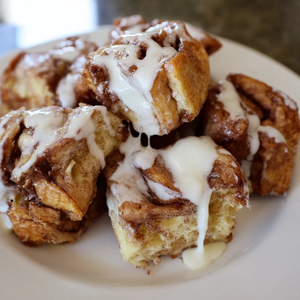 Golden-brown Cinnamon Roll French Toast Bites glistening with warm icing, served alongside fresh berries on a rustic breakfast plate.