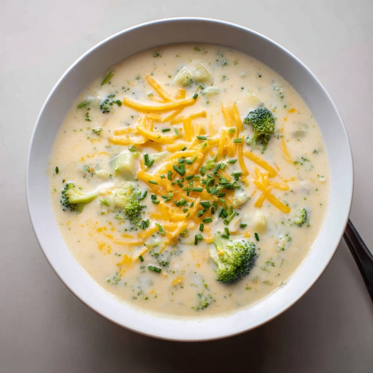 Vibrant broccoli florets and potato chunks swim in Creamy Cheesy Broccoli Potato Soup garnished with extra shredded cheddar.