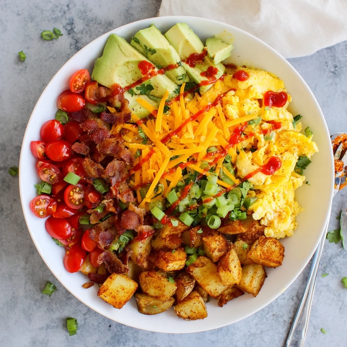 Golden scrambled eggs and crispy roasted potatoes topped with melted cheddar and bacon in a loaded breakfast bowl.