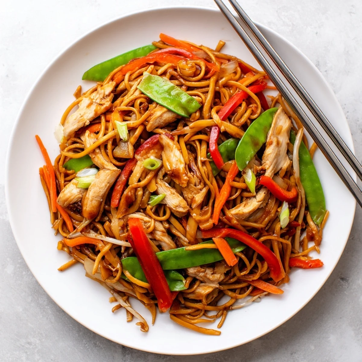 Hot wok of freshly tossed Chicken Chow Mein with julienned carrots, red bell peppers, and snow peas steaming invitingly.