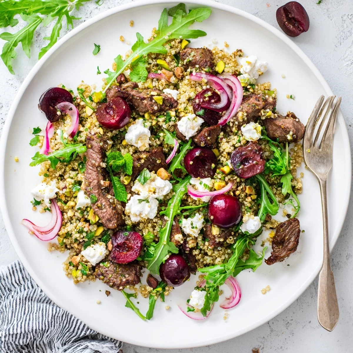 Golden spiced lamb strips nestled atop fluffy quinoa with ruby cherries and crumbled feta in a vibrant Mediterranean salad bowl