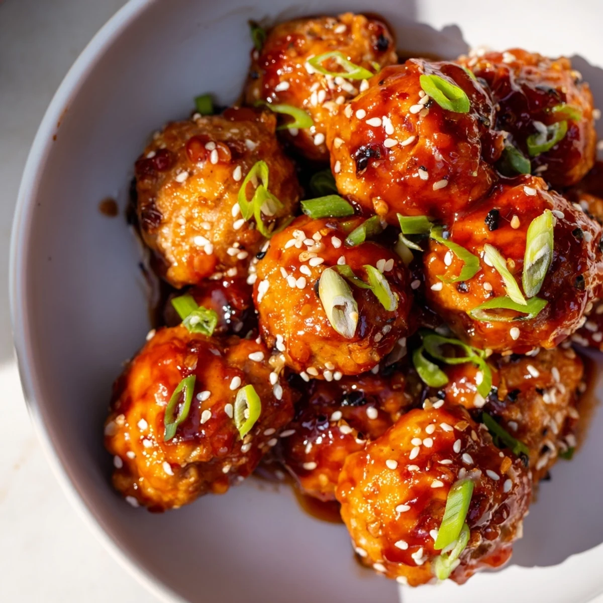 Juicy baked firecracker chicken meatballs coated in sticky tangy sauce and garnished with green onions