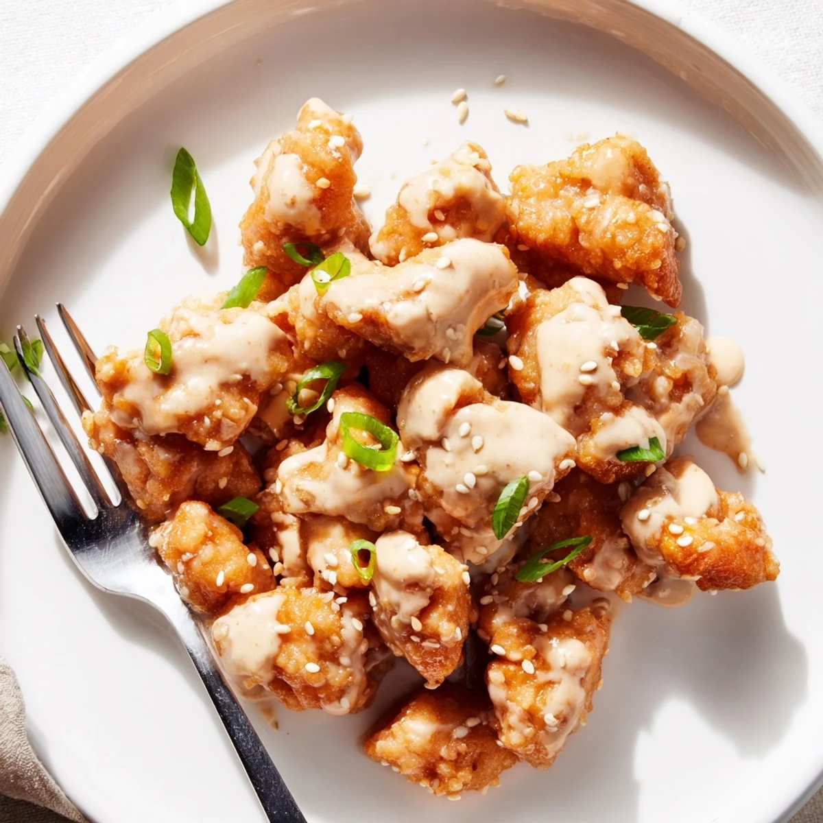 Crispy golden Bang Bang Chicken pieces coated in creamy red spicy sauce and garnished with green scallions