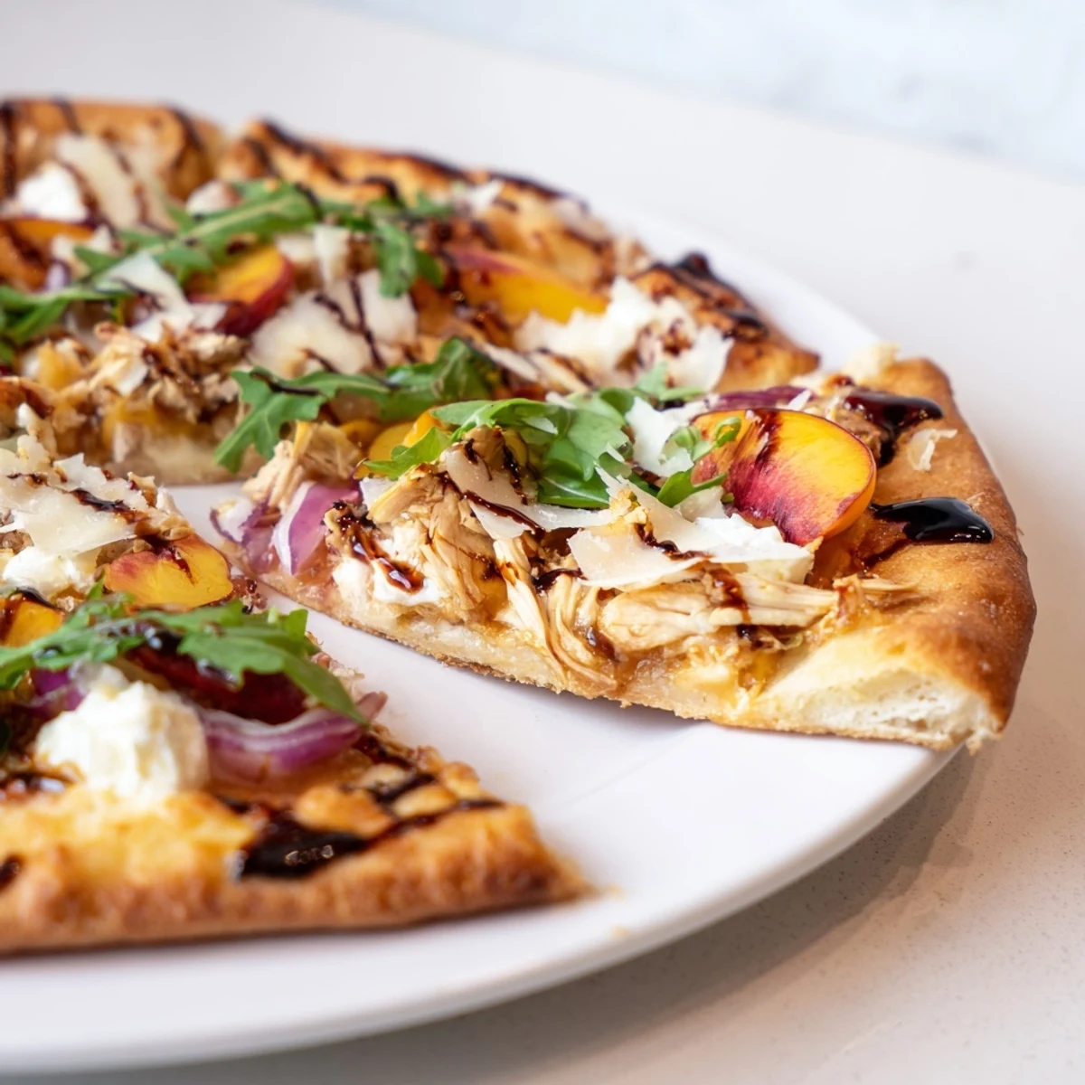 Golden chicken peach ricotta pizza topped with fresh arugula and drizzled with balsamic glaze
