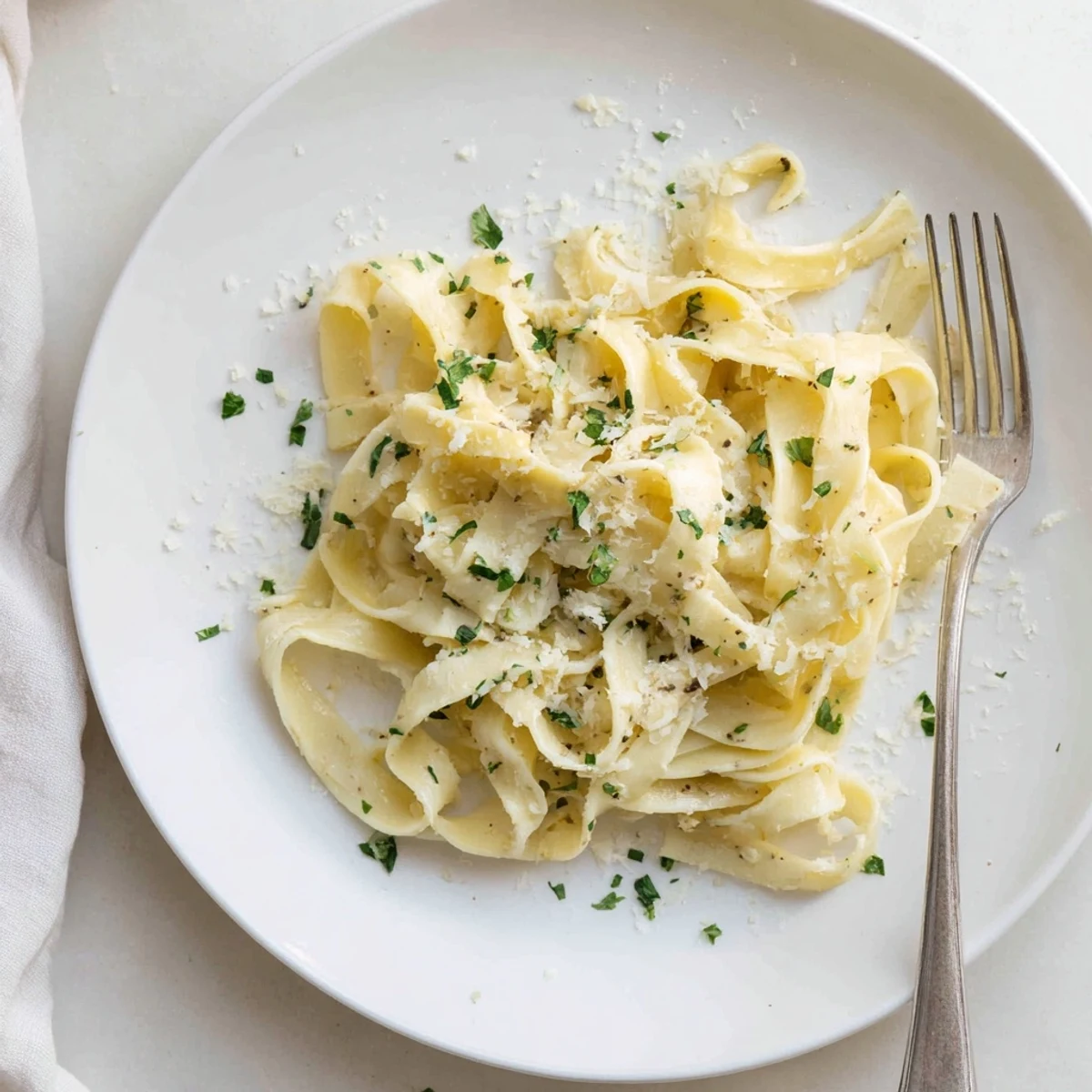 Steaming plate of fettuccine Alfredo drizzled with silky Parmesan cream sauce and fresh herbs