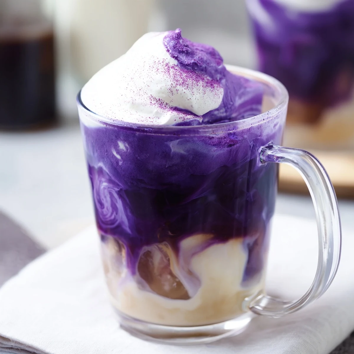 Steaming ube latte in a mug with purple yam flakes sprinkled on whipped cream
