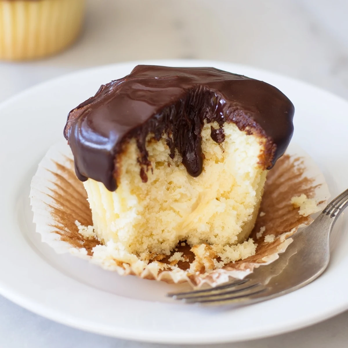 Fluffy vanilla cupcakes filled with creamy pastry cream beneath a rich chocolate glaze topping