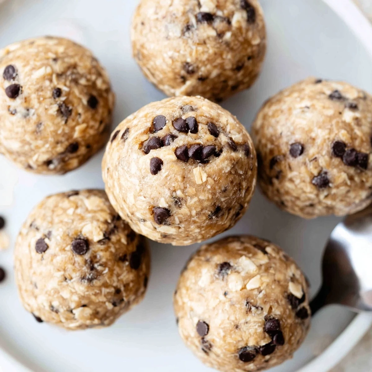 Bite-sized chocolate chip cookie dough protein balls rolled in mini dark chocolate chips on a white plate