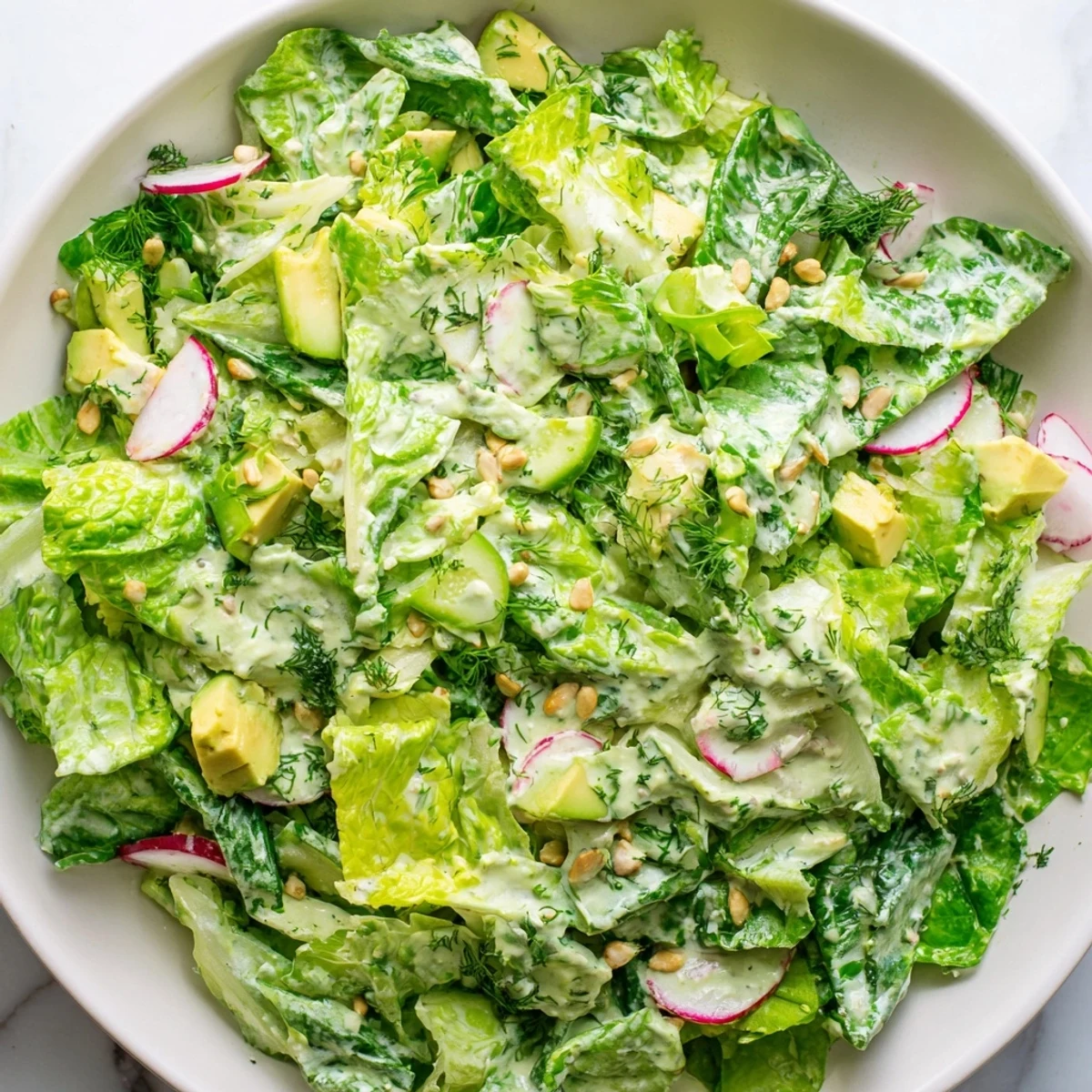 Hearty bowl of fresh Green Goddess Salad showcasing layered crunchy vegetables, creamy avocado cubes, and smooth green dressing coating.