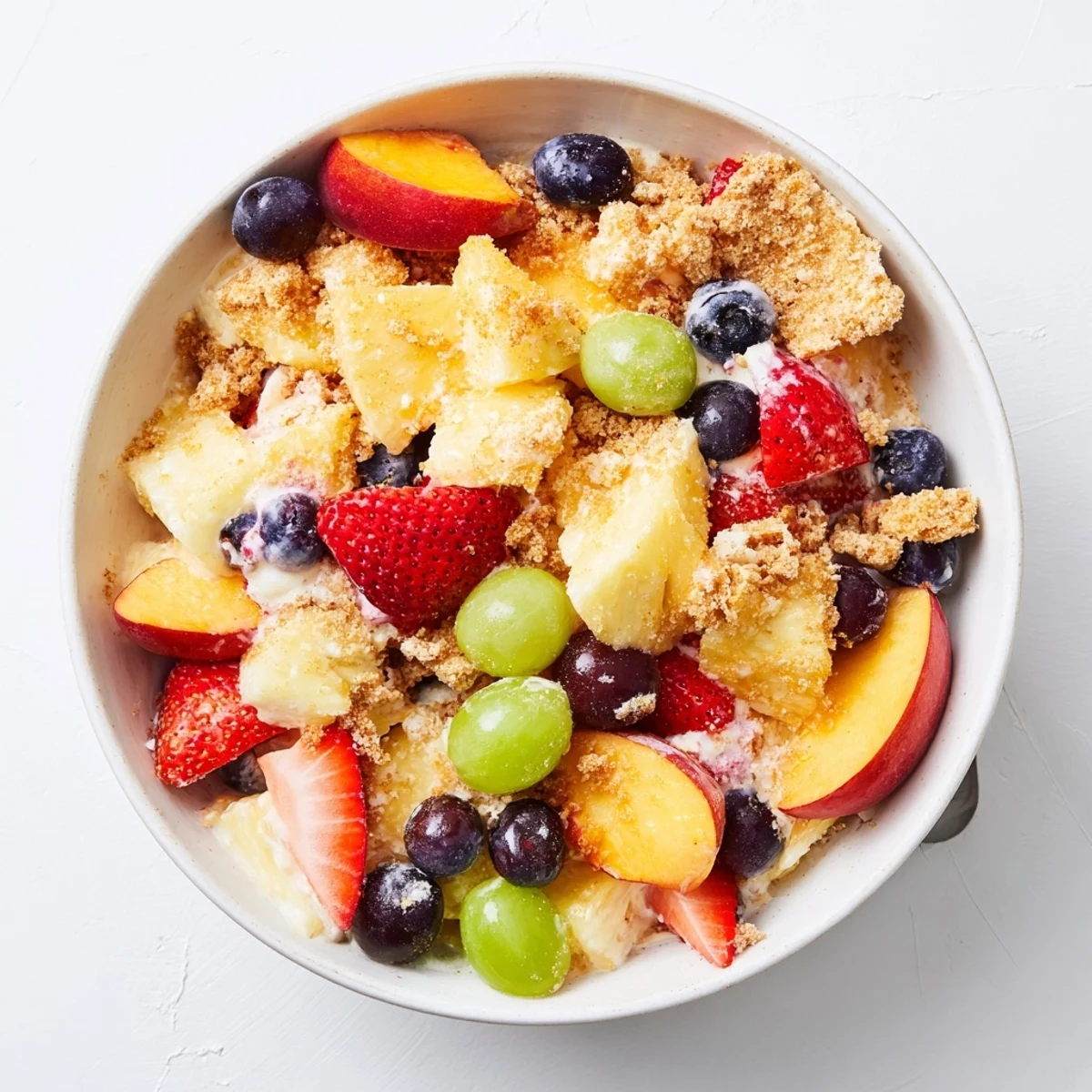 Colorful bowl of peach cobbler cheesecake fruit salad featuring juicy peaches, strawberries, and sweet cheesecake coating