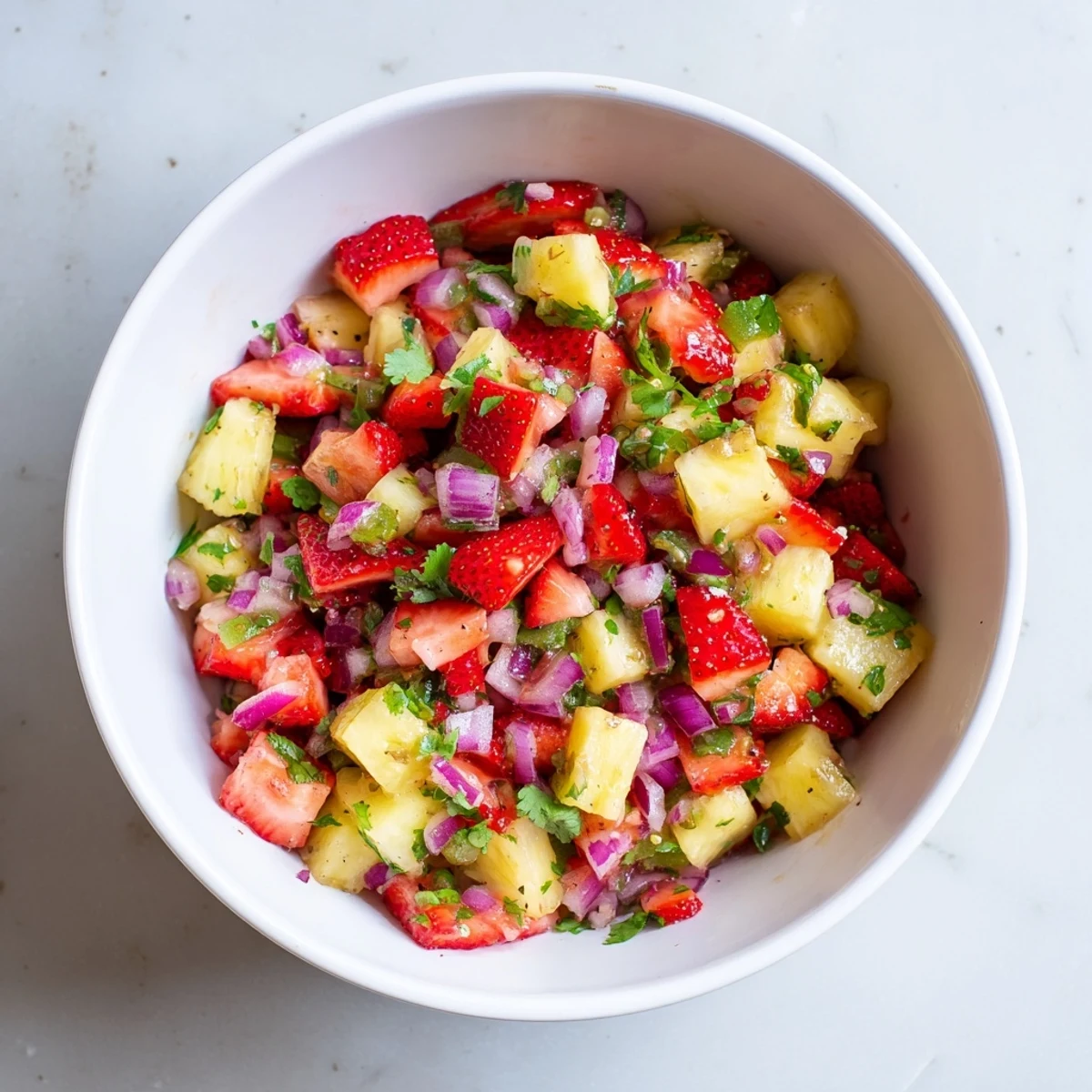 Fresh strawberry pineapple salsa in white bowl with red strawberries yellow pineapple green cilantro and chips