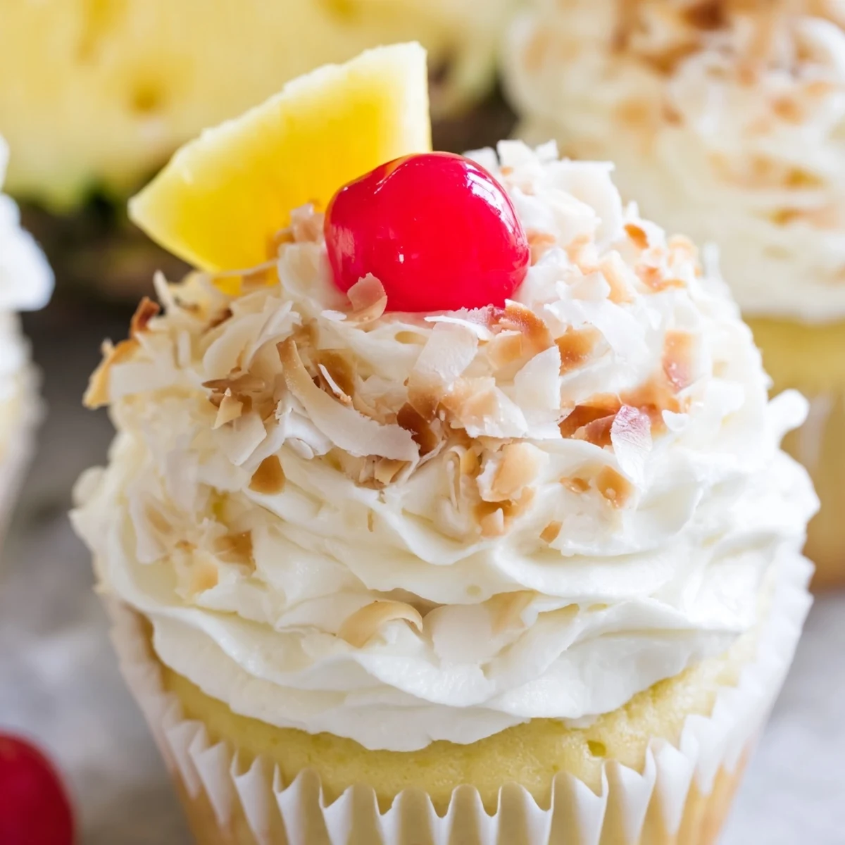 Festive Pina Colada cupcakes with rum infused sponge and swirls of coconut frosting, decorated with maraschino cherries and pineapple
