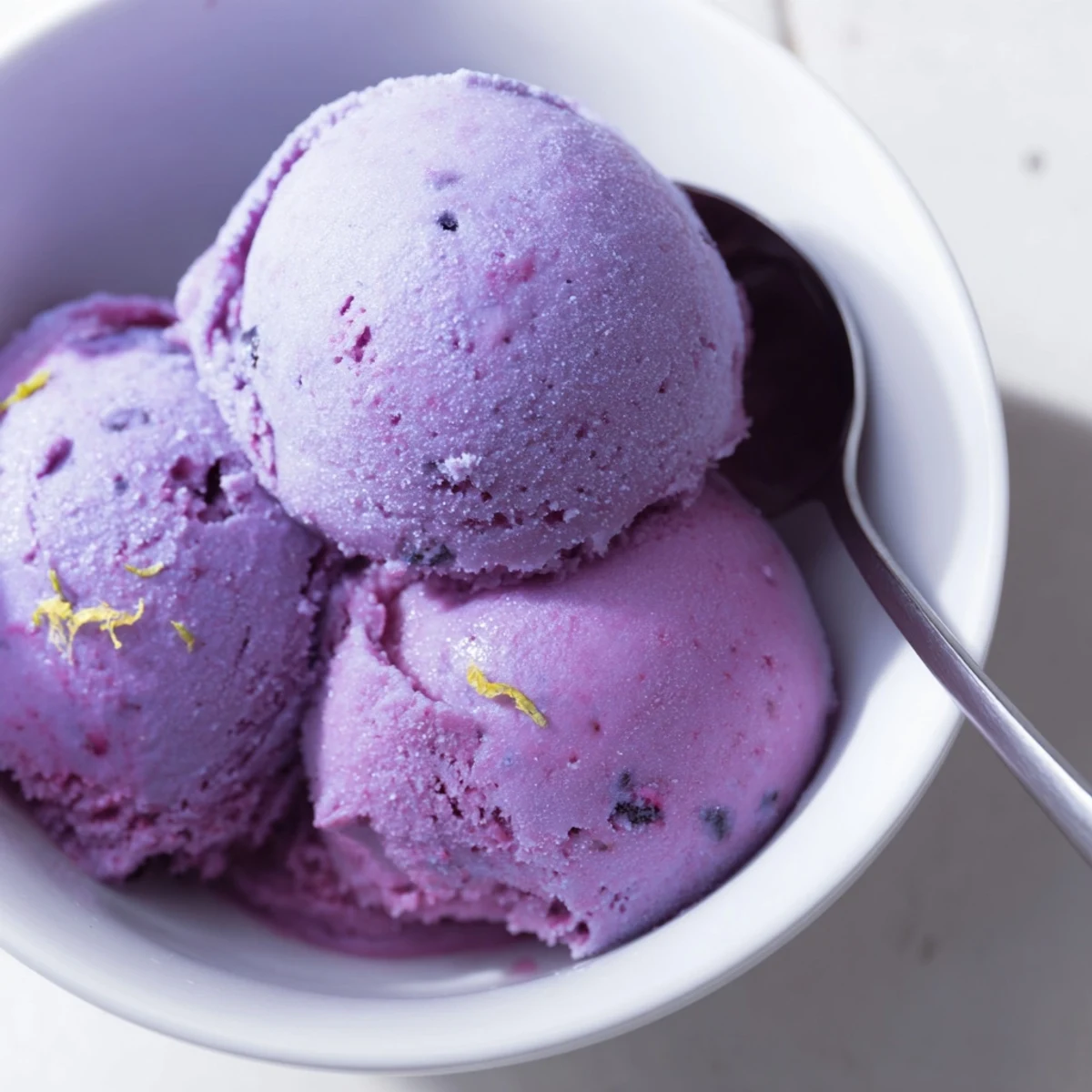 Creamy smooth no churn blueberry lemon sorbet melting slightly in a white dessert bowl topped with lemon zest