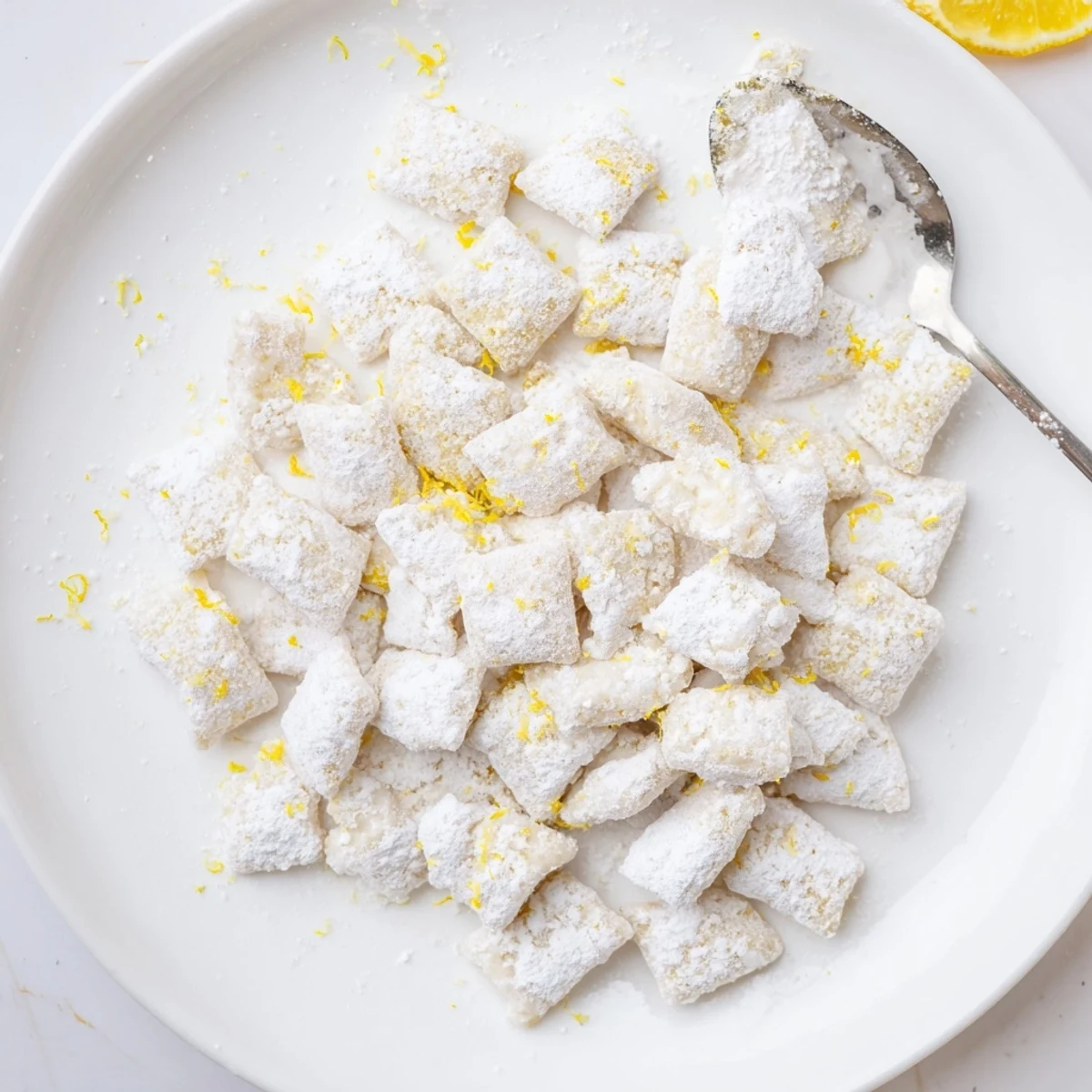 Zesty lemonade puppy chow snack scattered on baking sheet with bright lemon zest garnish