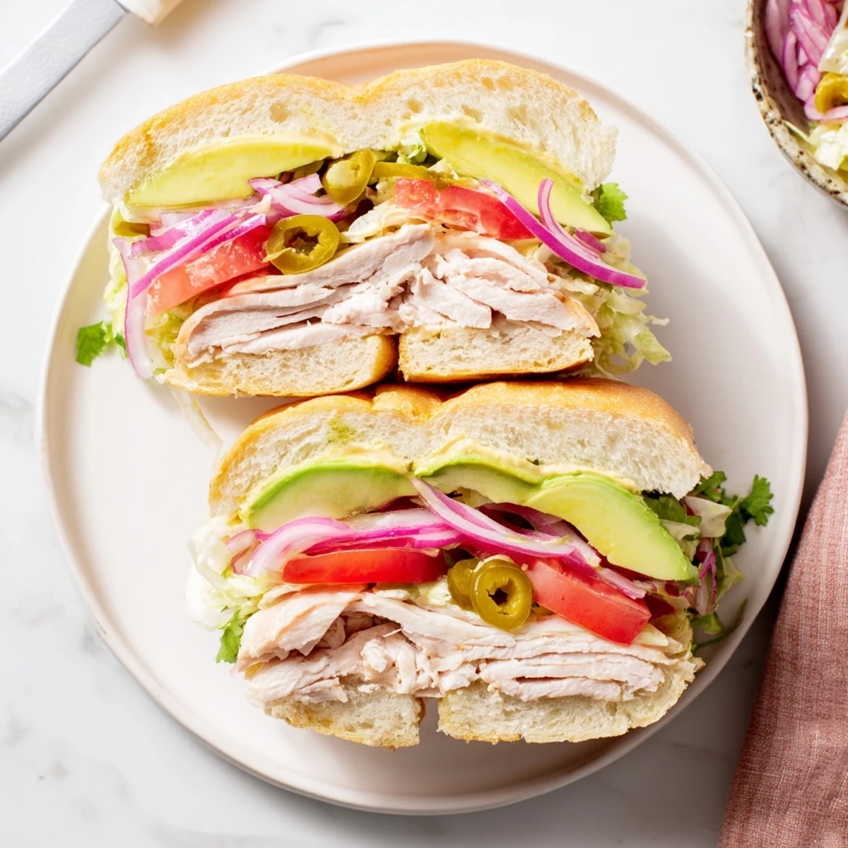 Chicken Torta Sandwich piled high with marinated chicken, creamy avocado slices, and crisp vegetables on a toasted bolillo roll