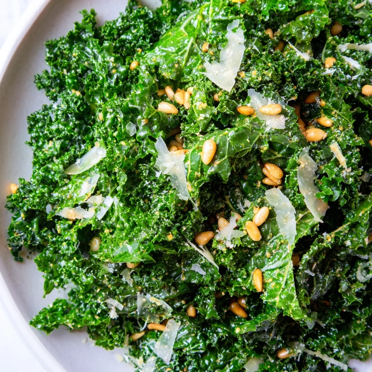 Bright green Garlic Lemon Parmesan Kale Salad topped with shaved cheese and toasted pine nuts