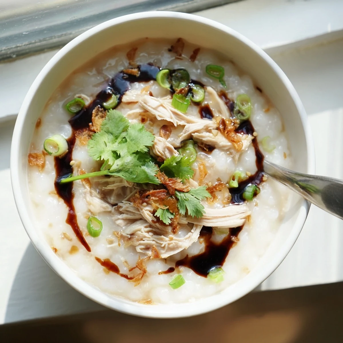 Steaming hot chicken congee garnished with crispy fried shallots and drizzled sesame oil