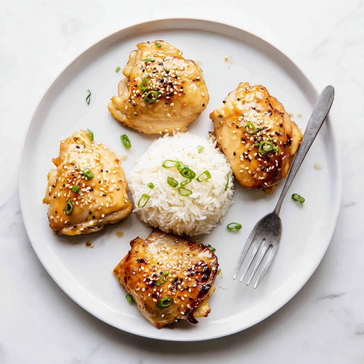 Glazed Honey Garlic Chicken on white plate, sesame seeds and scallions glistening