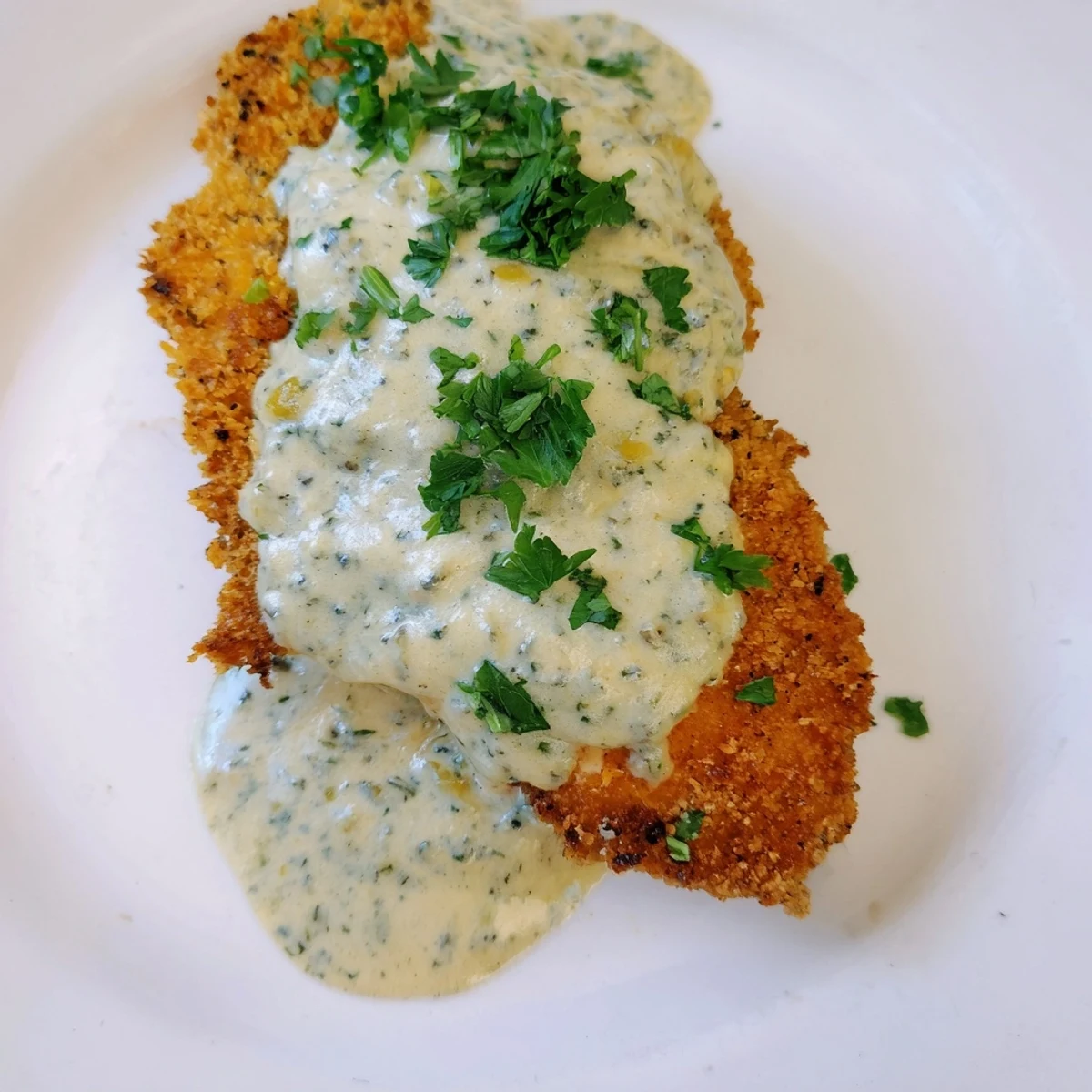 Pan-fried crispy chicken with juicy meat topped with smooth garlic cream sauce and fresh parsley