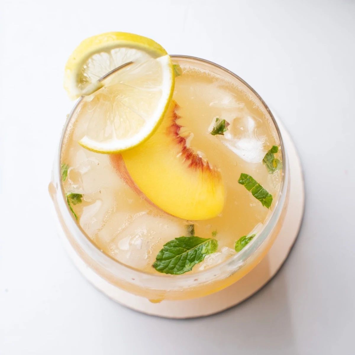 Refreshing summer peach lemonade drink garnished with mint leaves and citrus wheels