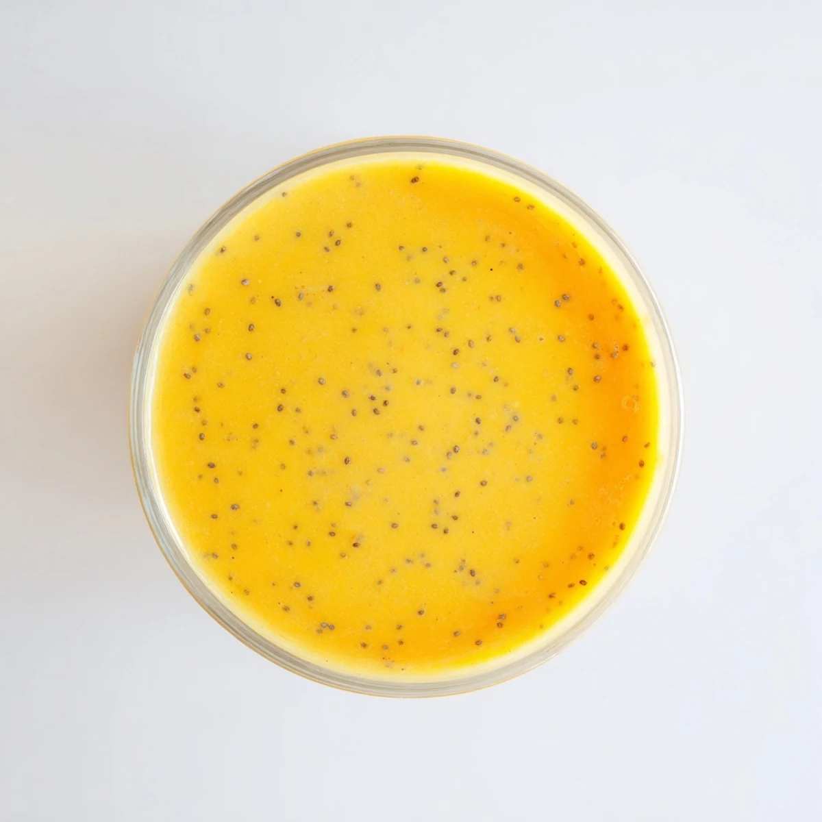 Tropical Sunrise Protein Smoothie featuring layers of bright orange mango pineapple blend topped with fresh fruit garnish in a clear glass showing creamy texture