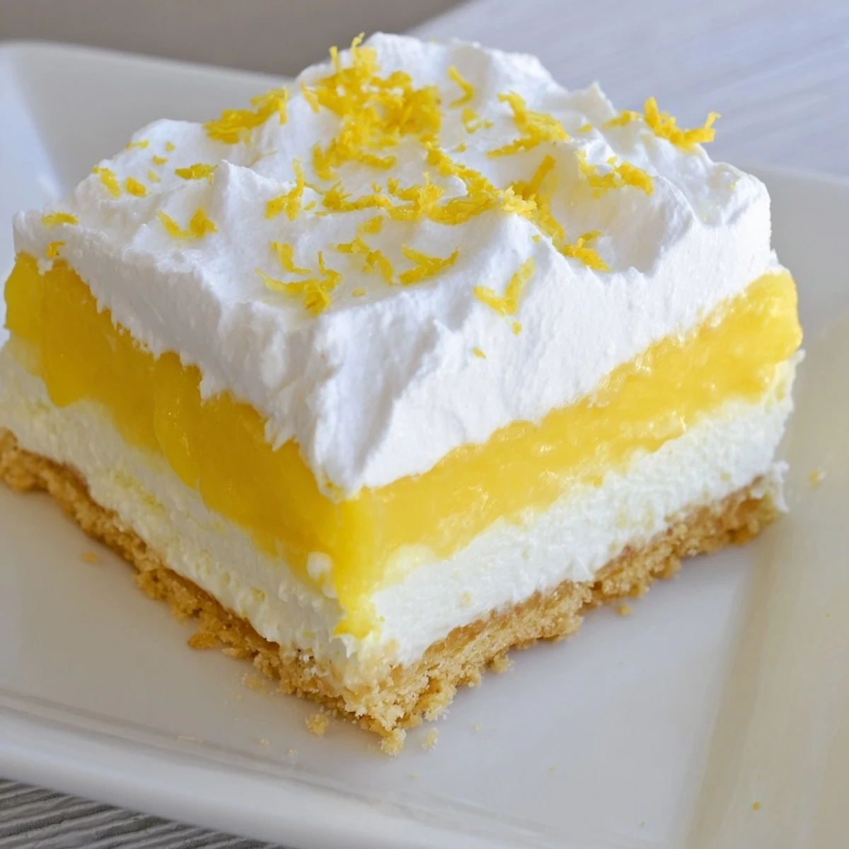 Golden square of lemon lush cake with creamy layers topped with fluffy white whipped cream