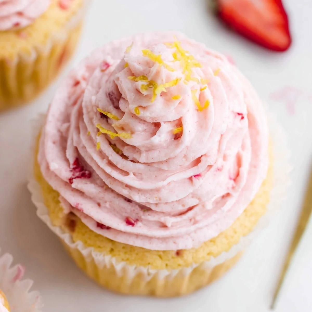 Moist strawberry lemonade cupcakes with fresh strawberry pieces and zesty lemon zest garnish on a wooden board