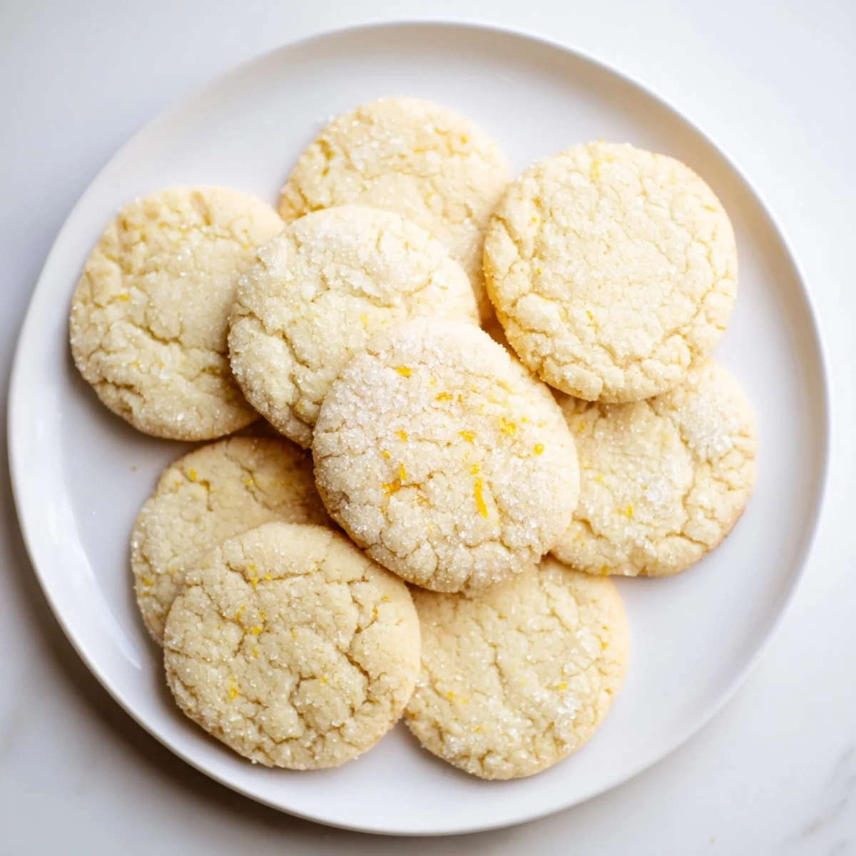 Soft chewy lemon cookies with golden edges and sugary coating on a white plate